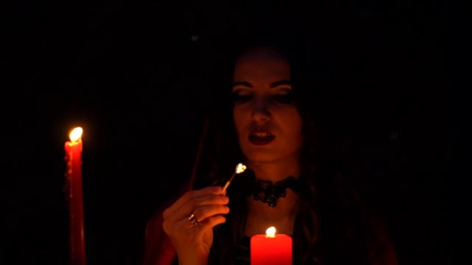 迷人的美丽黑发女巫，戴着红色斗篷的蜡烛，在神秘的秋天森林中让人联想到。带有心脏，鸡腿和豪猪针的巫术