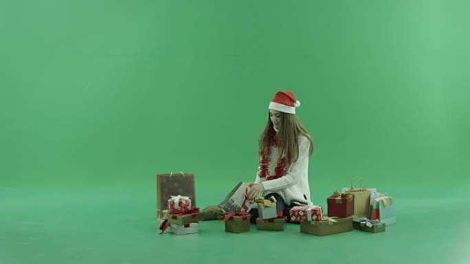 戴着圣诞礼帽的年轻美女看着她的圣诞礼物和购物袋，背景上的色键