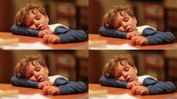 困倦的孩子累了，头在桌子上睡着了。漫长的一天后睡觉的小男孩，从一天的活动中筋疲力尽