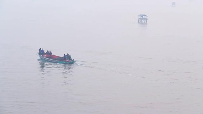 渔民骑着蓝色船在早晨雾蒙蒙的时候钓鱼。在进入大海之前，渔民在河口的海中用竹子建造的传统房屋的景色。