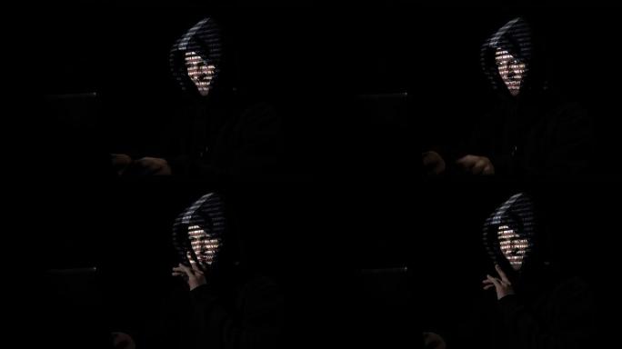 胡德中的坏黑客努力在黑暗的房间里从家里创建病毒，而代码反映在他的脸上