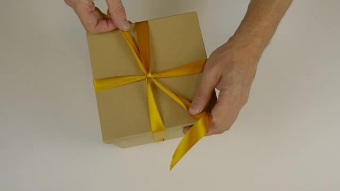 准备送礼。用金丝带包装的礼品盒。双手用黄丝带包裹礼品盒并鞠躬。特写俯视图高角度。