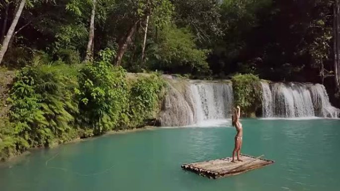 无人机射击-竹筏上的年轻女子在雨林的瀑布上拥抱自然，张开双臂的人们旅行度假概念。4k分辨率，菲律宾