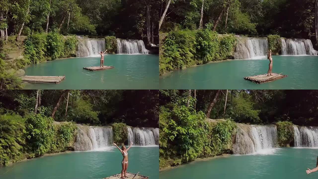 无人机射击-竹筏上的年轻女子在雨林的瀑布上拥抱自然，张开双臂的人们旅行度假概念。4k分辨率，菲律宾