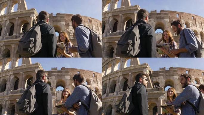 三个年轻的朋友游客站在罗马斗兽场前阅读地图指南指向背包太阳镜快乐美丽的女孩长发慢动作