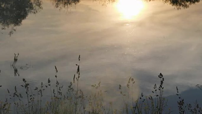 日落-天空中的日落及其在河流水表面的反射。夏夜。前景中的烟杆