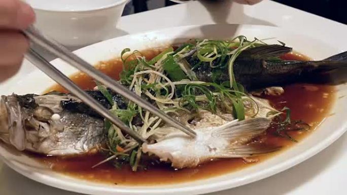 女人在餐厅吃香草和蔬菜蒸鲈鱼的动作