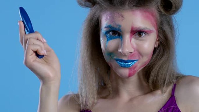 多色舞台化妆的高级时尚金发模特展示蓝色睫毛膏管。时尚视频。