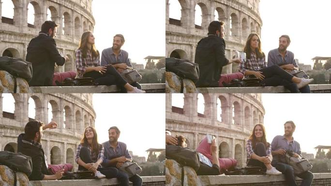 日落时坐在罗马斗兽场前的三个年轻朋友游客阅读地图指南指向背包太阳镜快乐美丽女孩长发慢动作