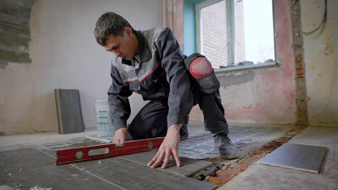 师傅穿着工作服，正在检查安装瓷砖的地平线，使用建筑水平，调整