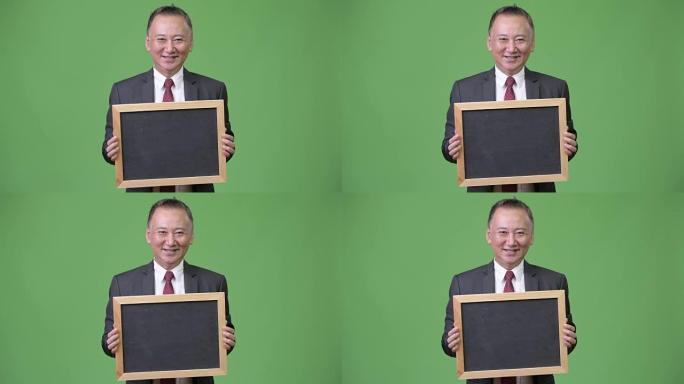 成熟的日本商人在绿色背景下拿着黑板