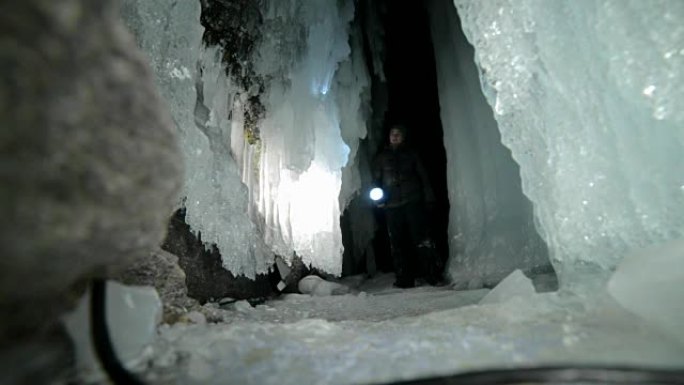 贝加尔湖冰洞上的旅行者。去冬日岛旅行。背包客正在冰上行走。旅行者看着美丽的冰窟。徒步旅行者穿着银色夹