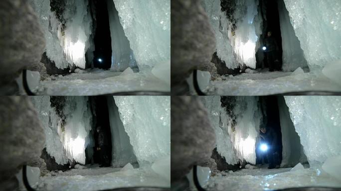 贝加尔湖冰洞上的旅行者。去冬日岛旅行。背包客正在冰上行走。旅行者看着美丽的冰窟。徒步旅行者穿着银色夹