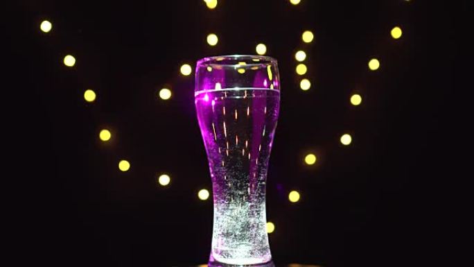 淡紫色灯下的一杯水正在旋转。丁香鸡尾酒。酒吧概念