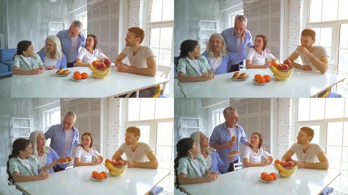 端着水果坐在餐桌旁的大家庭。慢动作