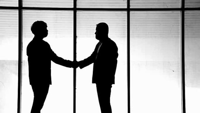 两个商人在现代化的办公室里握手。剪影拍摄