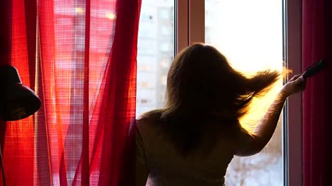 女孩一大早站在窗前梳头。太阳的光线穿过玻璃照亮了房间，女孩带着晨光