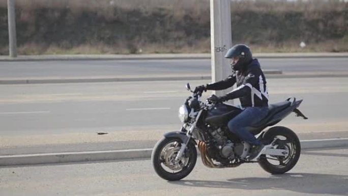 年轻有魅力的男子摩托车手，戴着黑色头盔和运动摩托车在街上