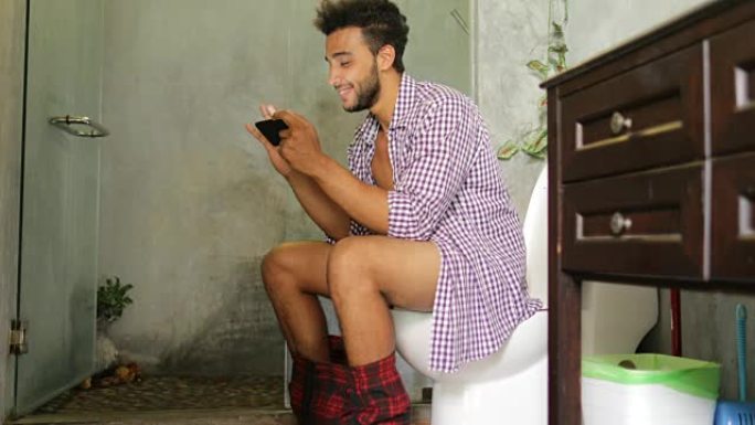 坐在马桶上的男人使用手机智能手机年轻拉丁家伙玩游戏