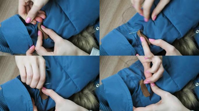 女人的手将皮革插入到蓝色夹克上。厚织物很难穿针。