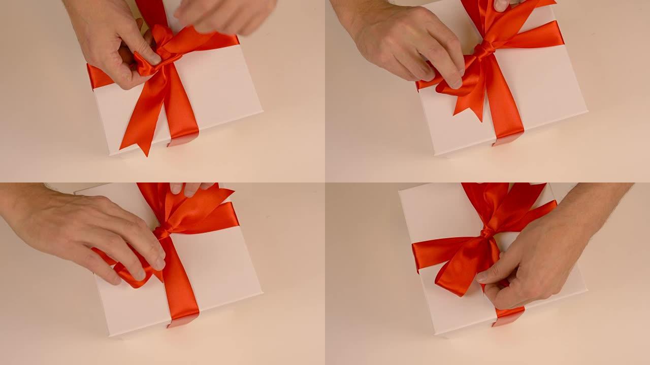特写俯视图高角度。男士双手伸直礼品盒上缎带上的红色蝴蝶结。为送礼活动做准备。带红色蝴蝶结的礼品盒。白