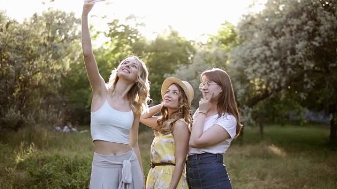三个年轻女性用手机自拍的前视图，摆姿势。女孩们在花园里花时间在户外。母鸡党的概念