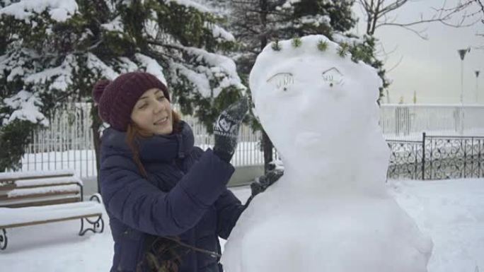 开朗的女人堆雪人，在户外享受冬天。