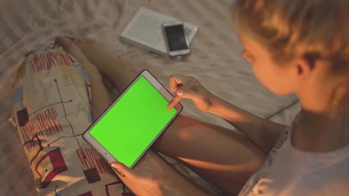 一个女孩坐在床上，使用带有色度键屏幕的平板电脑。刷卡。