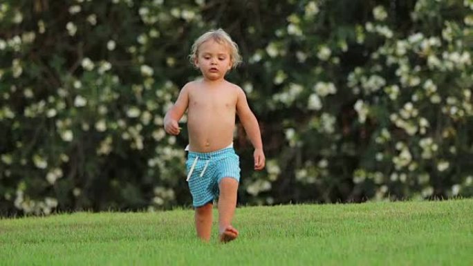 婴儿蹒跚学步的婴儿走向相机在60fps慢动作4k剪辑分辨率。蹒跚学步的婴儿在草坪草坪上走向相机