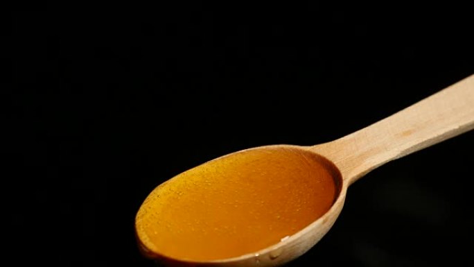 从黑色背景上的木勺上滴下来的蜂蜜
