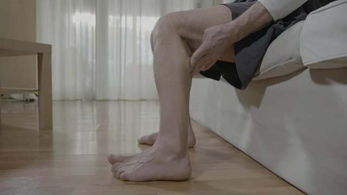 肌肉抽筋的退休男子坐在卧室里摩擦腿，治愈了令人不快的劳损