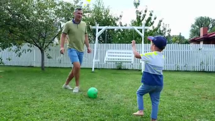 夏天，爸爸带着一个四岁的儿子在绿色草坪上的院子里打球，踢足球