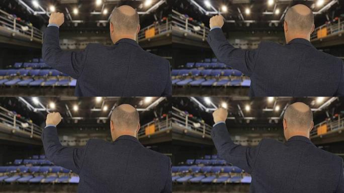 男人说话和移动握紧的拳头在前面的公众在大厅后视图