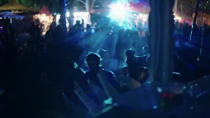 DJ在一个大型户外舞会上播放音乐，人们在跳舞