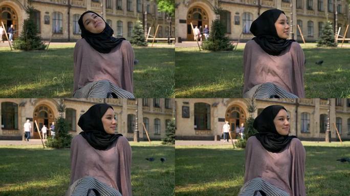 年轻美丽的穆斯林女孩梦想家正坐在草坪上，建立背景，宗教观念，放松观念