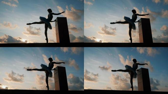 芭蕾舞短裙和尖角芭蕾舞演员的剪影在戏剧性的天空背景上。年轻漂亮的女人练习伸展运动。静态姿势的女孩。慢