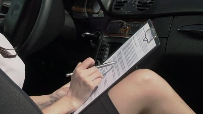 年轻的女商人坐在停放的汽车的前排座位上阅读文件