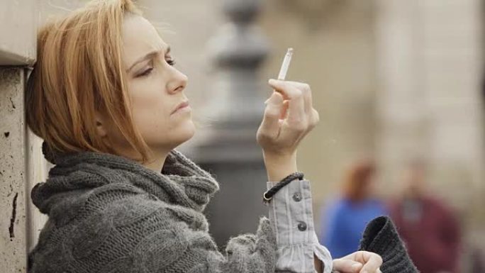 体贴悲伤的女人独自坐在城市街道边抽烟