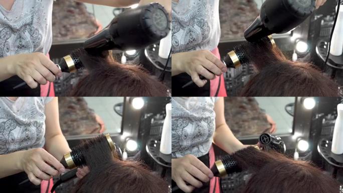 美发师-使用梳子和吹风机的发型师在美容院干燥并制作黑发女孩的头发。