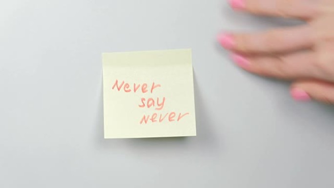 特写女人的手贴黄色贴纸纸，上面写着永远不要说永远。
