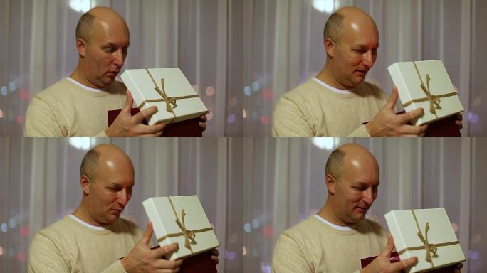 成年白人男子打开礼品盒并感到惊讶。一个惊讶而高兴的男人看着盒子里的礼物。闪烁的灯光照耀着他的脸。晚上