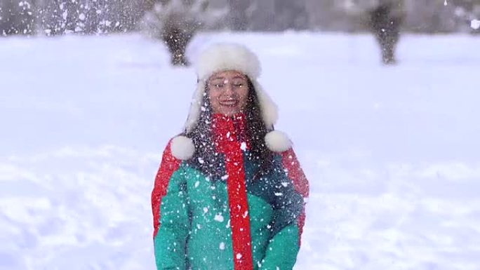 白雪皑皑的公园里的年轻幸福女人。女人用手把雪扔到空中。一个女人正在雪地上摔倒。
