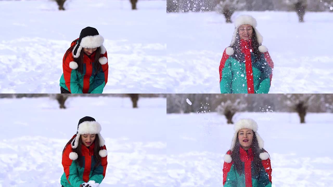 白雪皑皑的公园里的年轻幸福女人。女人用手把雪扔到空中。一个女人正在雪地上摔倒。