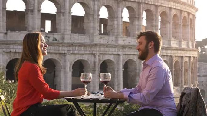 夕阳西下时，一对浪漫的情侣坐在罗马斗牛场前的餐厅桌前，喝着红酒互相敬酒
