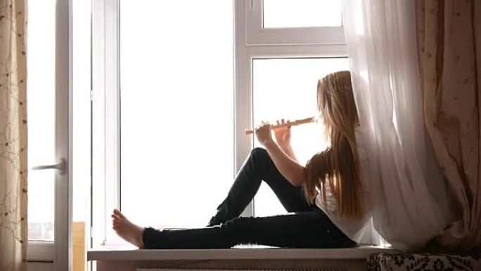年轻可爱的少女坐在家里的窗台上吹长笛