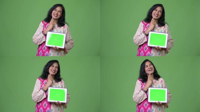 成熟快乐美丽的印度女人在展示数字平板电脑时思考