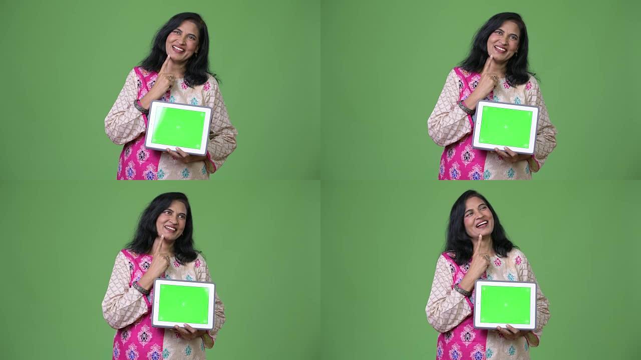 成熟快乐美丽的印度女人在展示数字平板电脑时思考