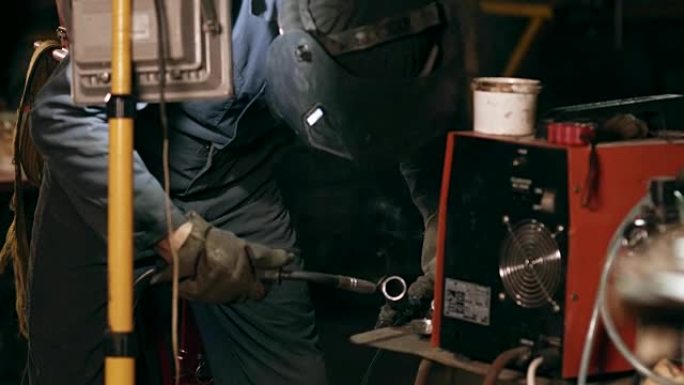 防护玻璃的男工人在机械机库将两个金属片焊接在一起。