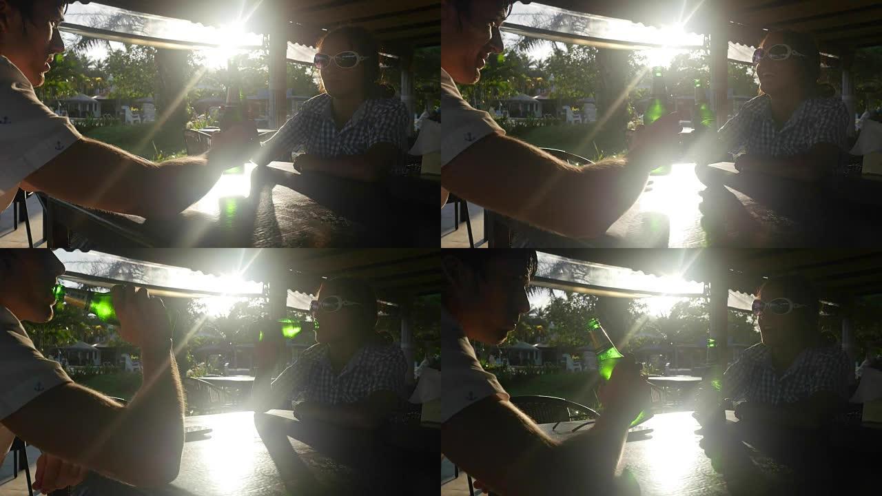 幸福的夫妇在太阳下山时在咖啡馆里用镜头闪光效果在阳光下叮叮当作响的啤酒瓶。3840x2160，全高清