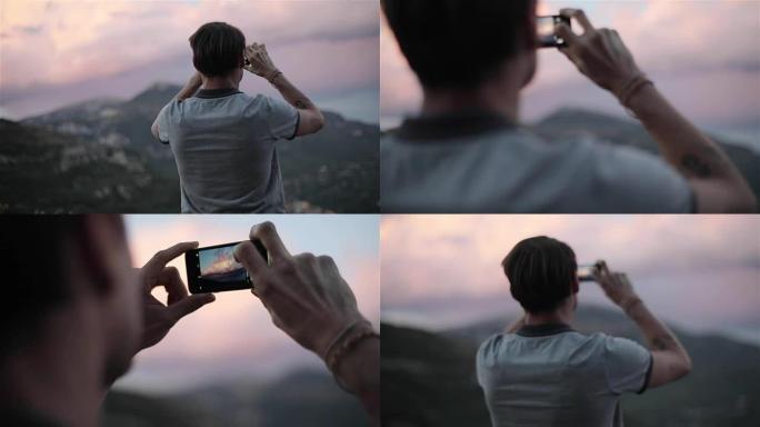 男性旅行者用电话拍照粉红色的云朵在山上的天空慢动作特写从背面和侧面机架聚焦，寻找图片触摸屏幕聚焦享受